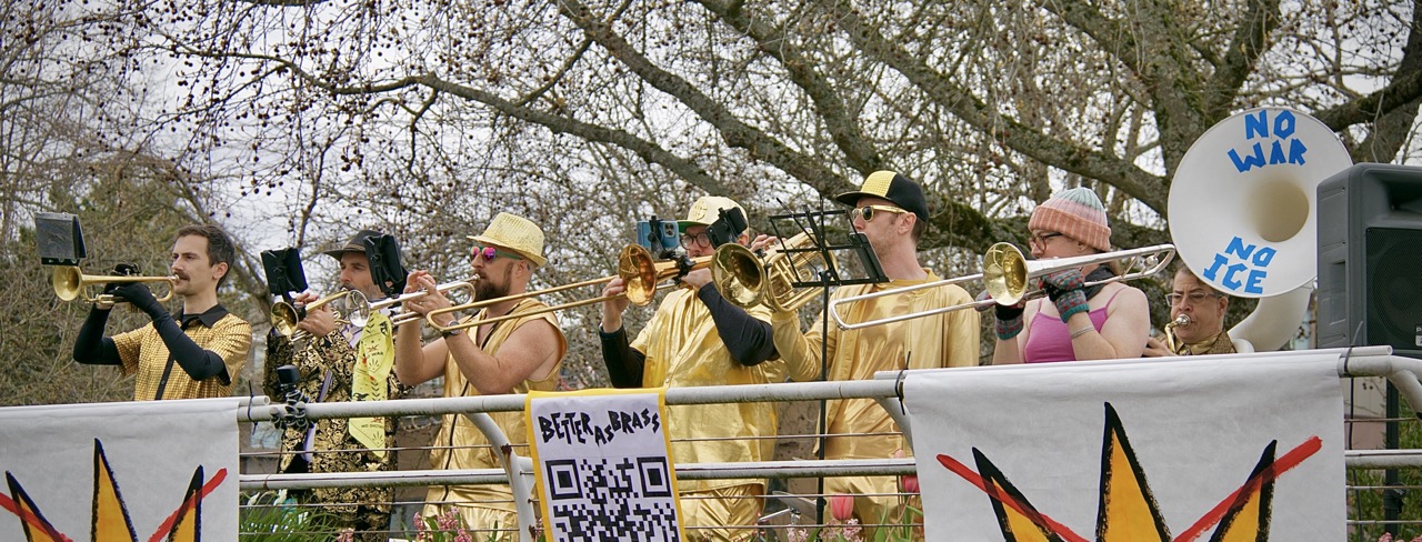 People dressed in metallic gold clothes playing brass instruments over a railing at an outdoor event.